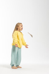 Portrait of beautiful cute little toddler girl. Child with funny face in yellow sweatshirt plays with hats. Pretty smile kid in studio on white background. High quality photo