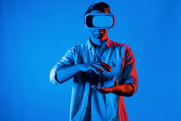 Caucasian smart man holding and moving gesture while using VR goggle. Happy person using headset and goggle while enter virtual world or metaverse with neon light background. Technology. Deviation.