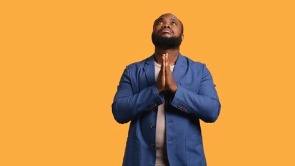 Pious african american man praying to his god, asking for forgiveness. Spiritual BIPOC man doing worship hand gesturing, confessing, begging for pardon, isolated over studio background, camera B