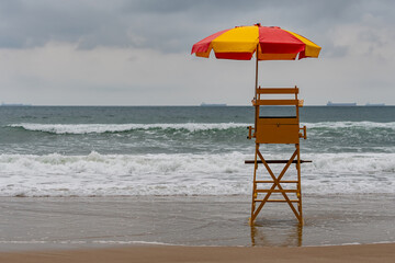 An empty lifeguard chair in front of a tourist beach that has strong waves. Tombo beach, Guaruja - SP- Brazil.