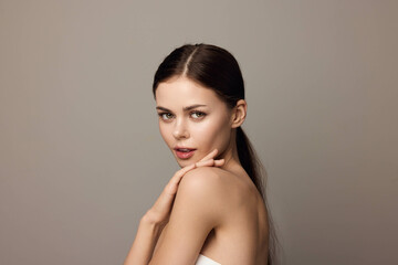 Beautiful young woman with long hair posing in front of a gray background, with her hands on her chin and looking at the camera