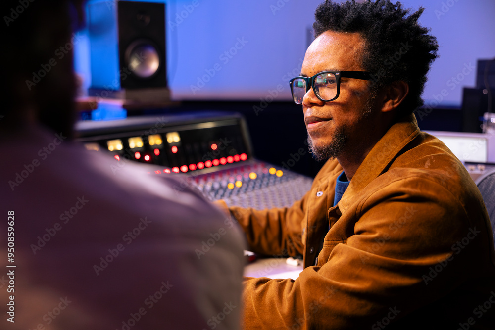 Poster Audio technician and artist collaborating on music for pop rock album, processing and editing sounds with mixing console and software on computer. Singer works with producer for cool tracks.