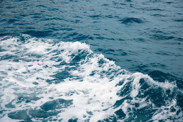 Wave on blue water and white foam on the tops of the waves from under the side of a floating boat, space for text