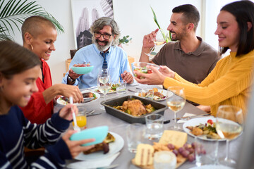 Smiling Caucasian family sitting at table passing food to each other at indoor festive event. Happy people of different generations enjoying lunch together at domestic life