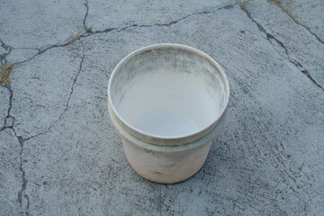 An empty, white plastic bucket sits on a cracked, gray concrete surface.