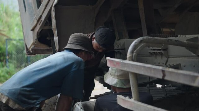 slow motion three young brothers mechanics working as a team under a truck in a family business