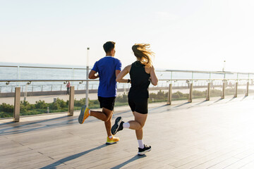 A couple running together on a sunlit boardwalk by the sea, embracing the ocean breeze and morning...
