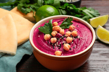 Tasty beetroot hummus in bowl and products on wooden table, closeup