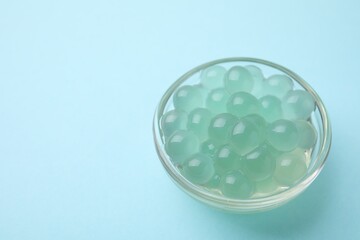 Bright tapioca pearls in bowl on light blue background, closeup. Space for text