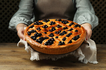 Woman holding tasty homemade pie with blueberries over wooden table, closeup