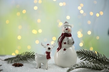 Cute decorative snowman and deer with fir branches on artificial snow