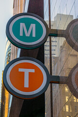Close-up of Train and Metro Sign, in Sydney, Australia. Round Green and Orange Signs with Letters T and M, attached to the entrance wall to a Train and Metro Station. Photo taken in July, 2024.