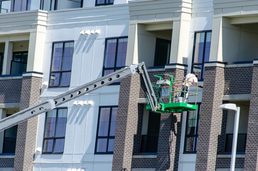 Construction Worker Painting on Boom Lift at Modern Apartment Building