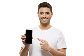 Young handsome man in white t-shirt holding phone, pointing to blank screen with finger,...