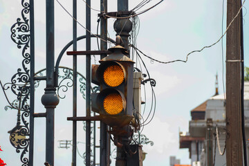 A close-up of a yellow caution traffic light framed by ornate ironwork, set against an urban...