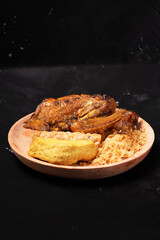 A plate of savory dishes including sweet grilled chicken with a dark brown color, fried tofu and tempeh, and crispy crumbs, served on a wooden plate against a dark background.