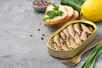 Tin can with sprats, bread, vegetables and herbs on a dark background, close-up. Horizontal, space...