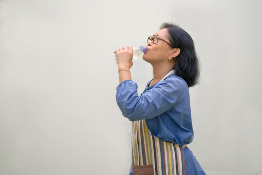 Side view: A woman wearing an apron is drinking water from a plastic bottle