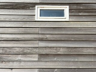 A window with a white frame in a grey wall made of wooden slats 
