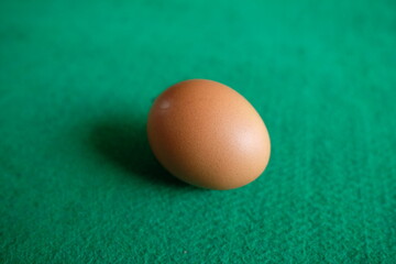 Close-up of a single brown egg on a green surface.