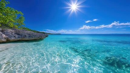 Fototapeta premium Serene beach scene with clear turquoise water, bright sun, and blue sky, perfect for relaxation and vacation themes.