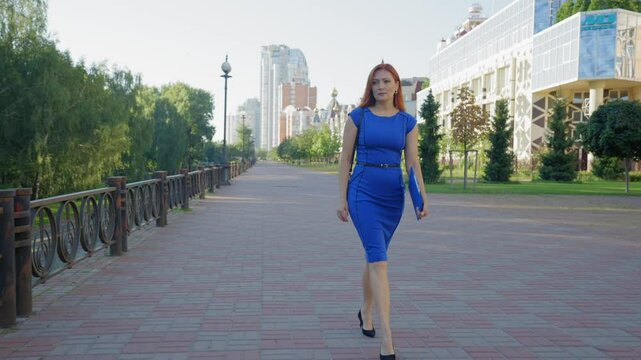Elegant beautiful redhead middle aged female entrepreneur in stylish high heels twisting her ankle , touching foot in pain while walking down city street,