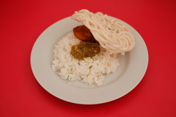 Rice with fried chicken and sambal in a white plate on a red background