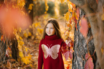 Cute baby girl with long hair in autumn in the park is smiling and enjoying a sunny day and good weather. Autumn walks and leisure for preschoolers