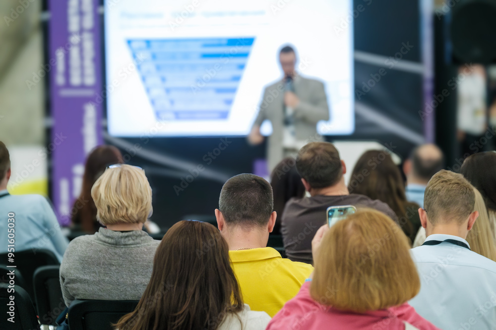 Wall mural Business professionals attending a conference presentation. Speaker giving lecture with slide presentation to engaged audience in a corporate event setting.