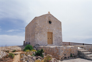 Malta - July 1, 2008: Summer view of stairs and entrance door of a small stone church with cross on the roof