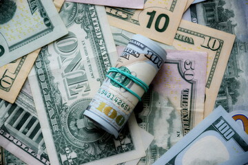 Hundred dollar bills roll lies on big amount of US dollars in different nominations under natural light