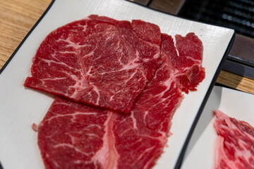 Korean Style Barbecue on plate in front of stainless grill. BBQ rare meat with soft focus