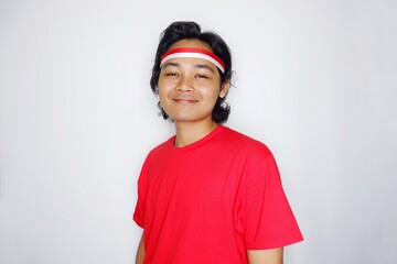 Portrait of an Indonesian man with long hair with a headband and red shirt celebrating Indonesian Independence Day with high nationalism on an isolated white background