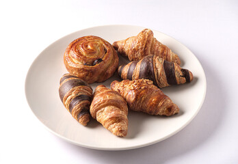 Croissants and Raisin Danish pastries, burnt brown, arranged on a white plate and white table.