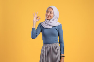 happy asian indonesian muslim woman giving ok finger gesture on isolated yellow background