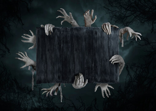 Mummy's hands wrapped in a bandage rises through the wooden boards. Background with copy space. The hand of the risen dead mummy monster for Halloween horror concept.