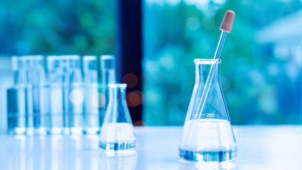 A captivating image featuring laboratory glassware, including a volumetric flask and a dropper, filled with clear liquid The soft blue background enhances the scientific atmosphere of the scene