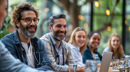 Fototapeta premium A diverse group of professionals smiling during a meeting in a modern, well-lit space. They are seated around a table with glasses of water and a laptop in front of them