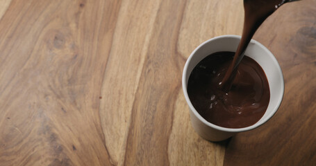 pour hot cocoa in paper cup on wood background with copy space
