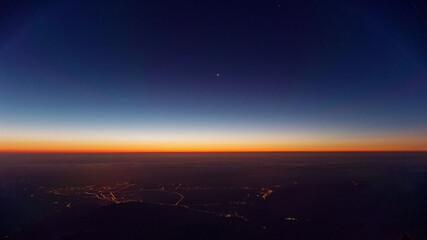 Stars on dark blue sky before sunrise, high angle view city light under mountains.