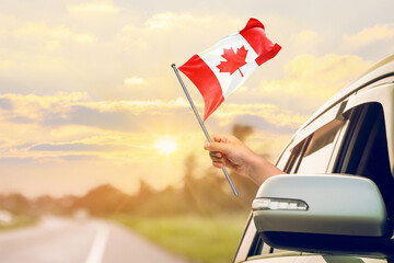 Waving the Canada flag against the sunrise or sunset from a car driving along a country road....