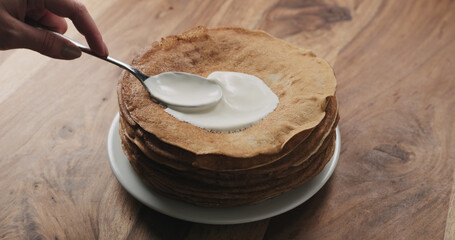 spreading sour cream on top of pancakes or blini