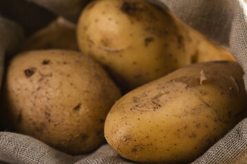 fresh raw potatoes in sack on wood background