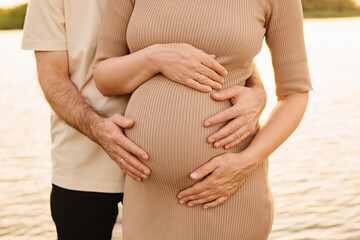 A man gently hugs a pregnant woman on the pier. 
