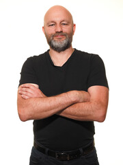 Portrait of a man in his 40s or 50s. Model is bald with grey beard in black shirt which shows his slim athletic body. White background. Healthy male posing. Hands crossed, smile on the face.
