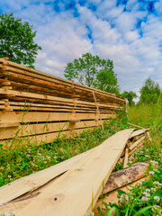 A pile of wood boards is sitting in a field with grass and trees in the background. The wood is stacked in a way that it looks like it's ready to be used for building. Construction industry