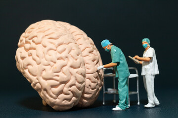 Miniature people of surgeons examining a large brain model. symbolizing the complexities of neuroscience and medical research