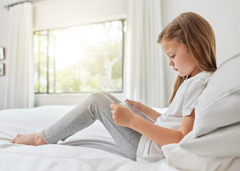 Obraz premium Little girl, reading and relax with tablet on bed for ebook, entertainment or online browsing at home. Young child, female person or kid with technology in bedroom for research, app or social media