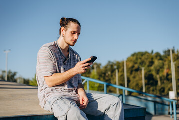 Focused person in casual clothes sitting on concrete surface and looking attentively at screen of cellular phone