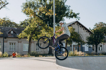 Fearless man in white helmet picking up speed while rising above skatepark slide and making flip in...